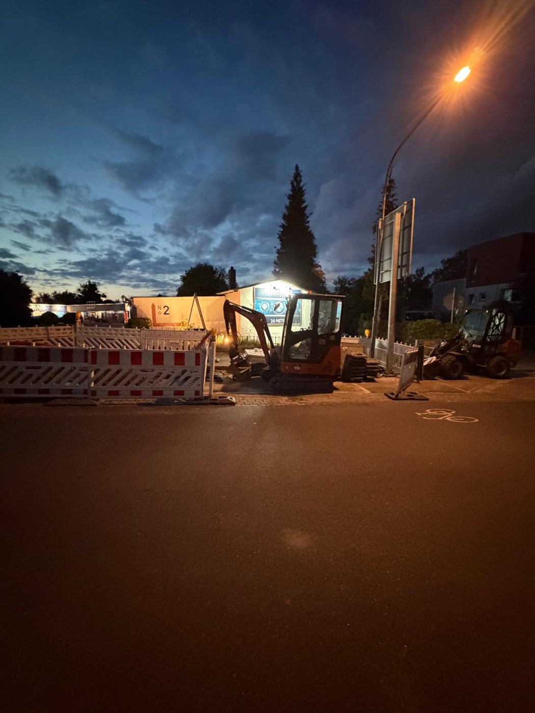 Minibagger und Baustellenabsperrung bei nächtlicher Straßenbeleuchtung